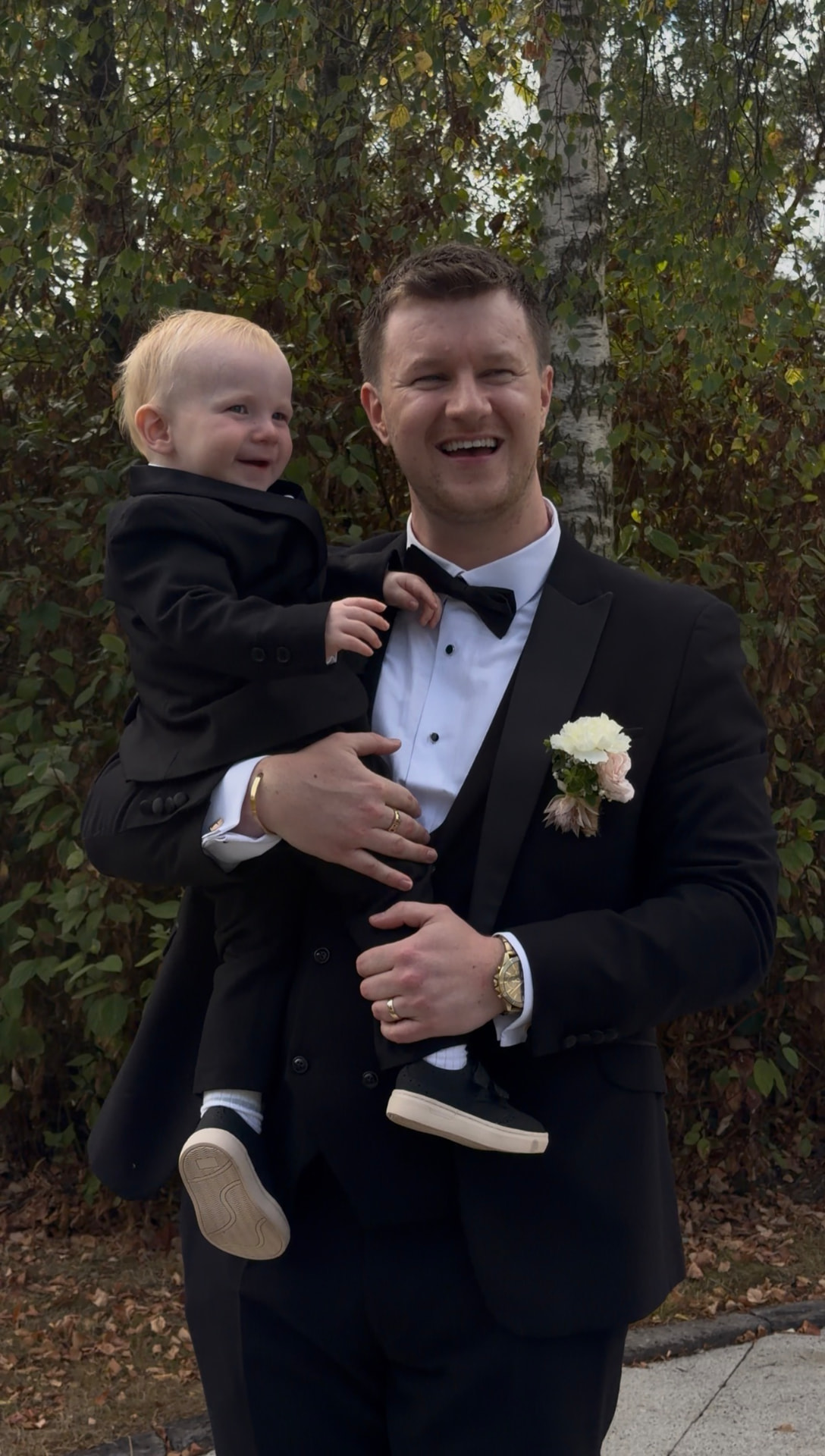 Thomas holding their son, both in matching tuxedos